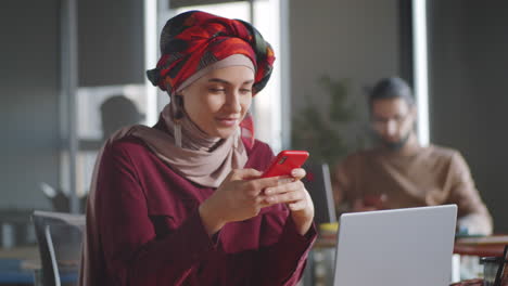 Hermosa-Mujer-En-Hijab-Enviando-Mensajes-De-Texto-En-El-Teléfono-Inteligente-En-La-Oficina